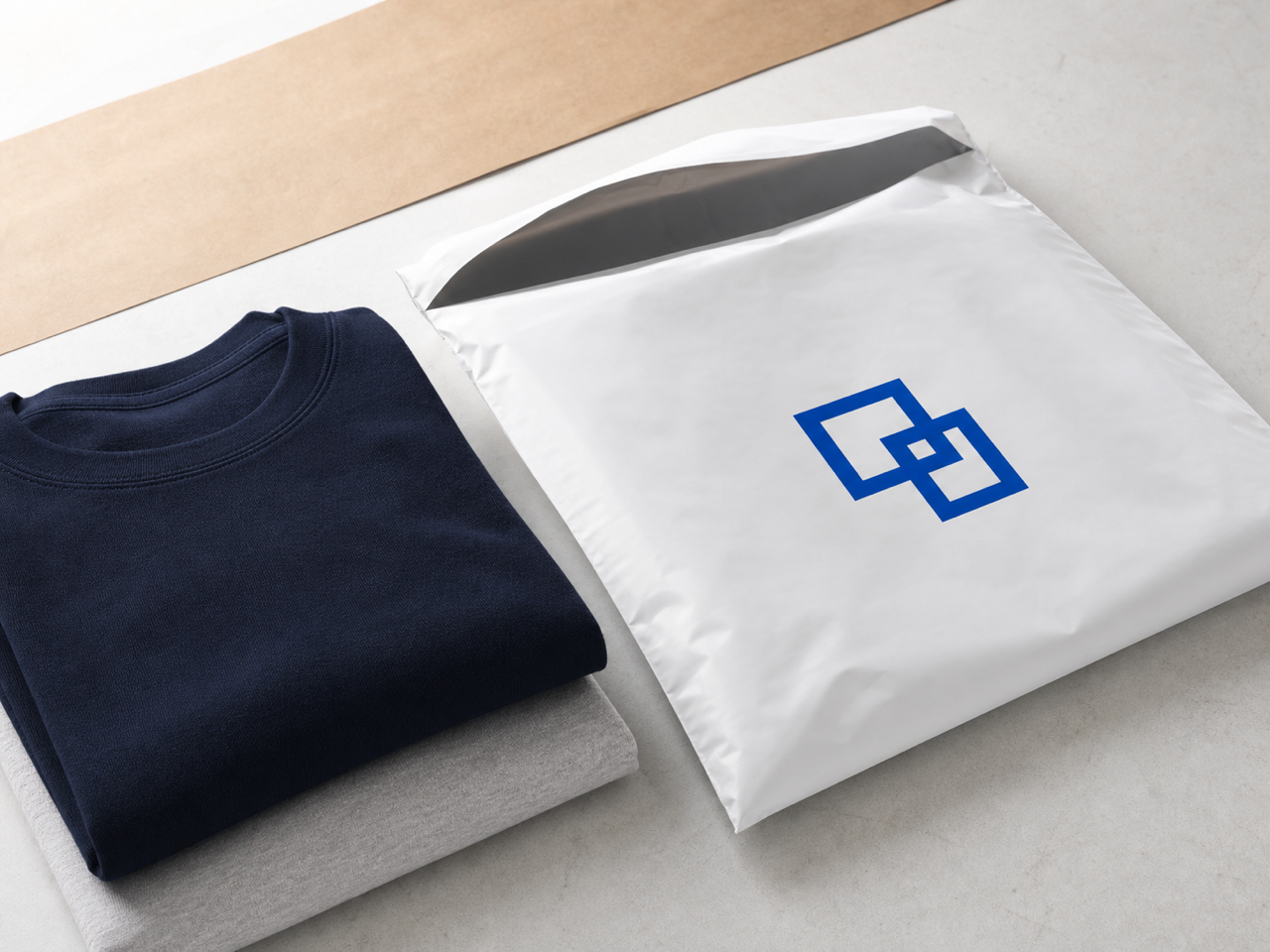 Folded navy and gray apparel beside an open custom white bio poly mailer