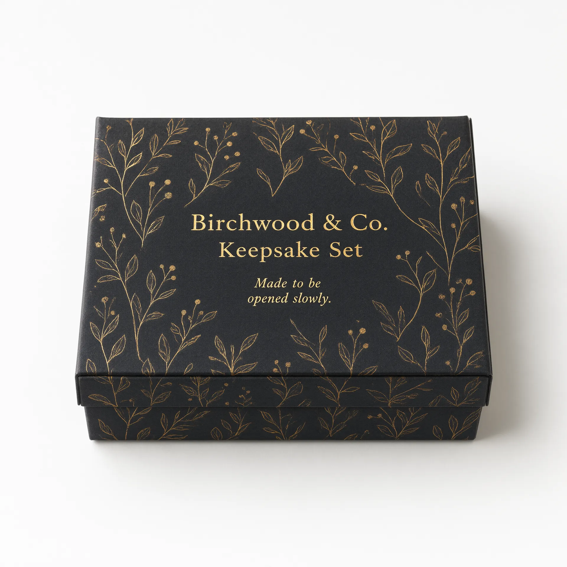 Closed small charcoal rigid box with a gold foil botanical motif, compact earring-box scale