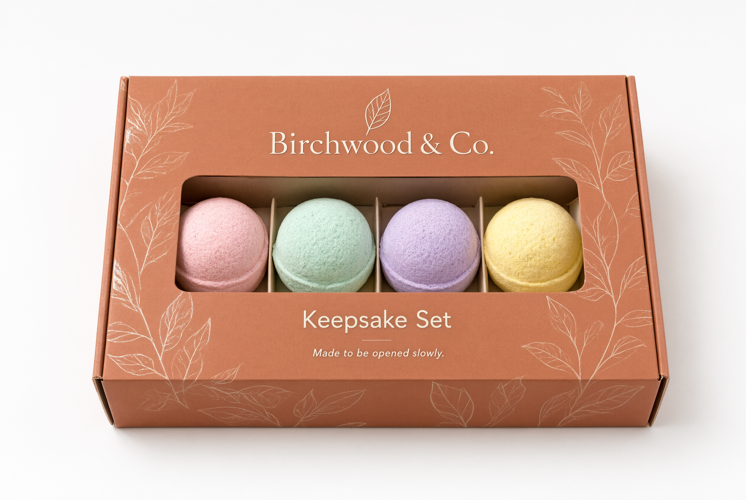Closed terracotta folding carton with a window showing four pastel-colored bath bombs inside