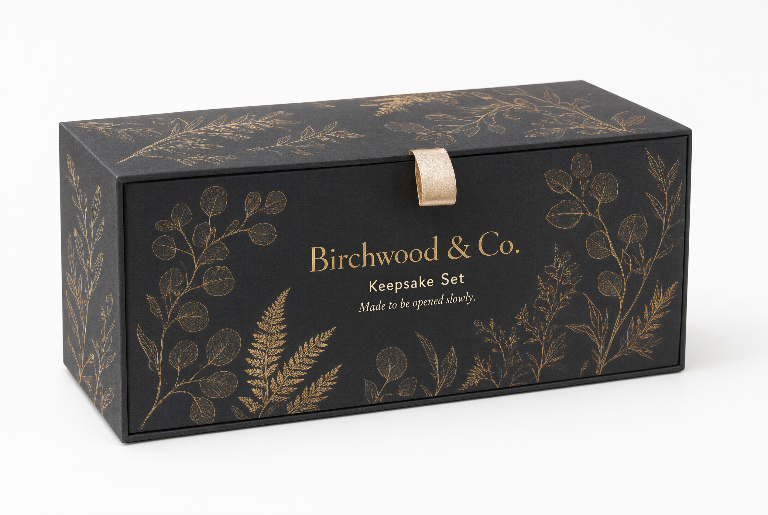 Closed charcoal drawer-style gift box with a gold foil botanical motif and ribbon pull