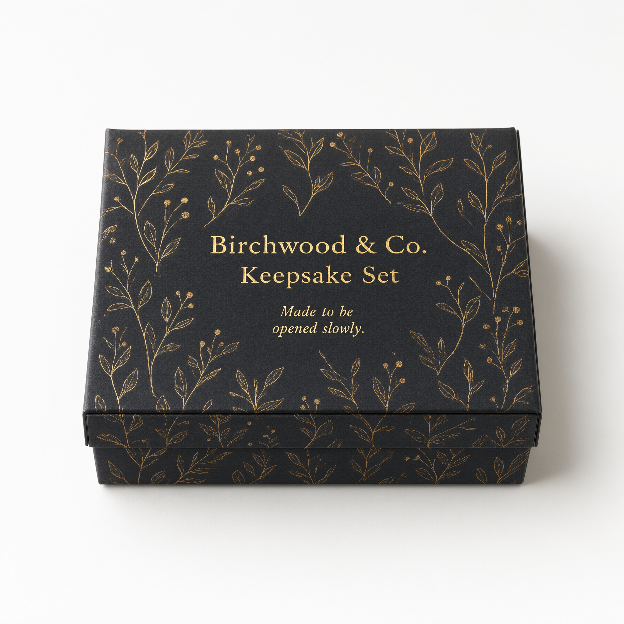 Closed small charcoal rigid box with a gold foil botanical motif, compact earring-box scale